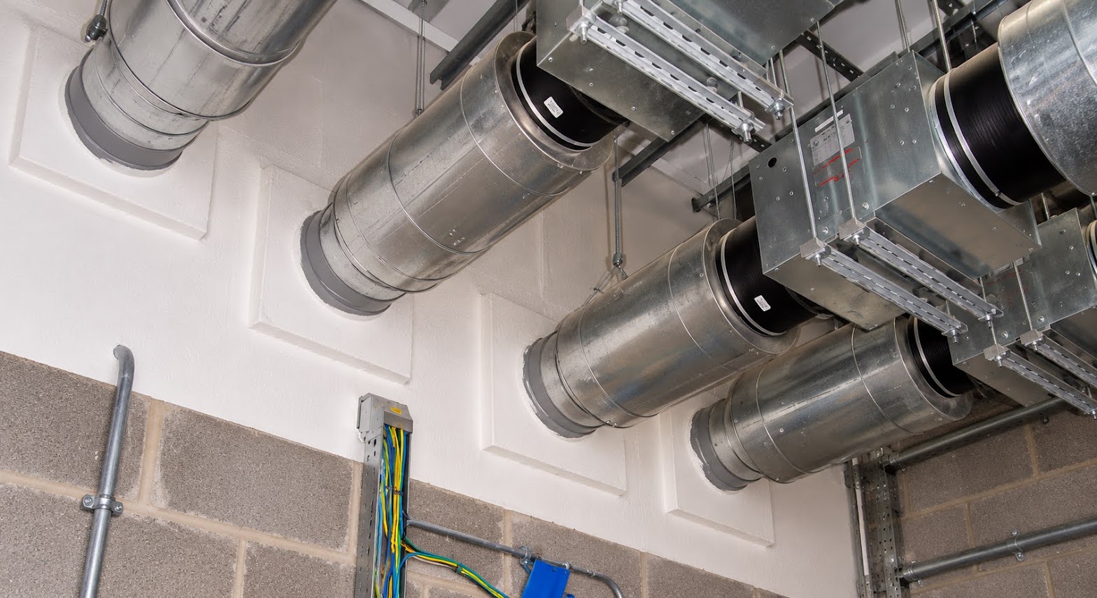 Ventilation ducts passing through a fire-resisting wall, each penetration neatly sealed with fire-rated boards