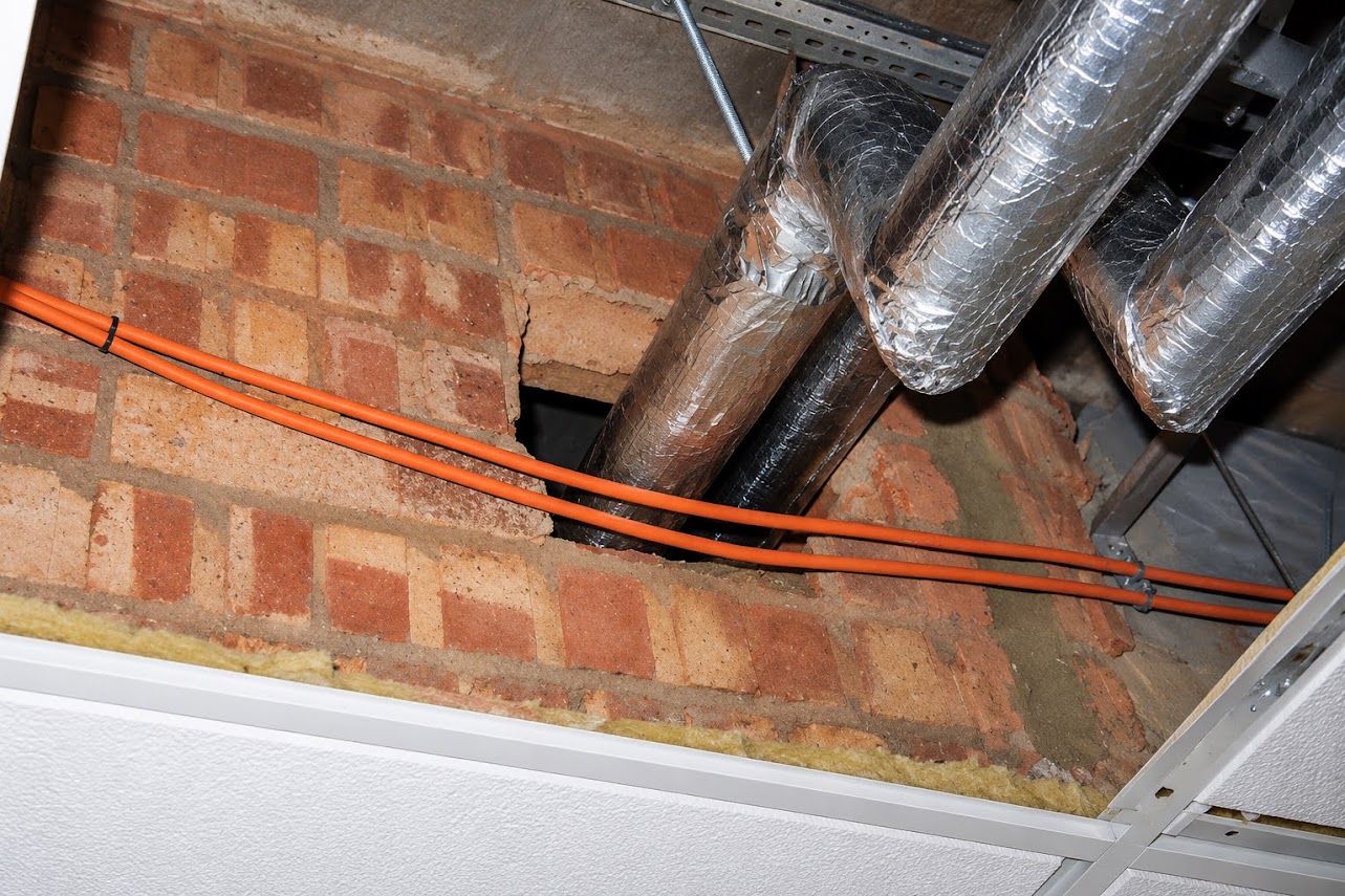 Ductwork and services passing through an opening in a blockwork wall above a suspended ceiling